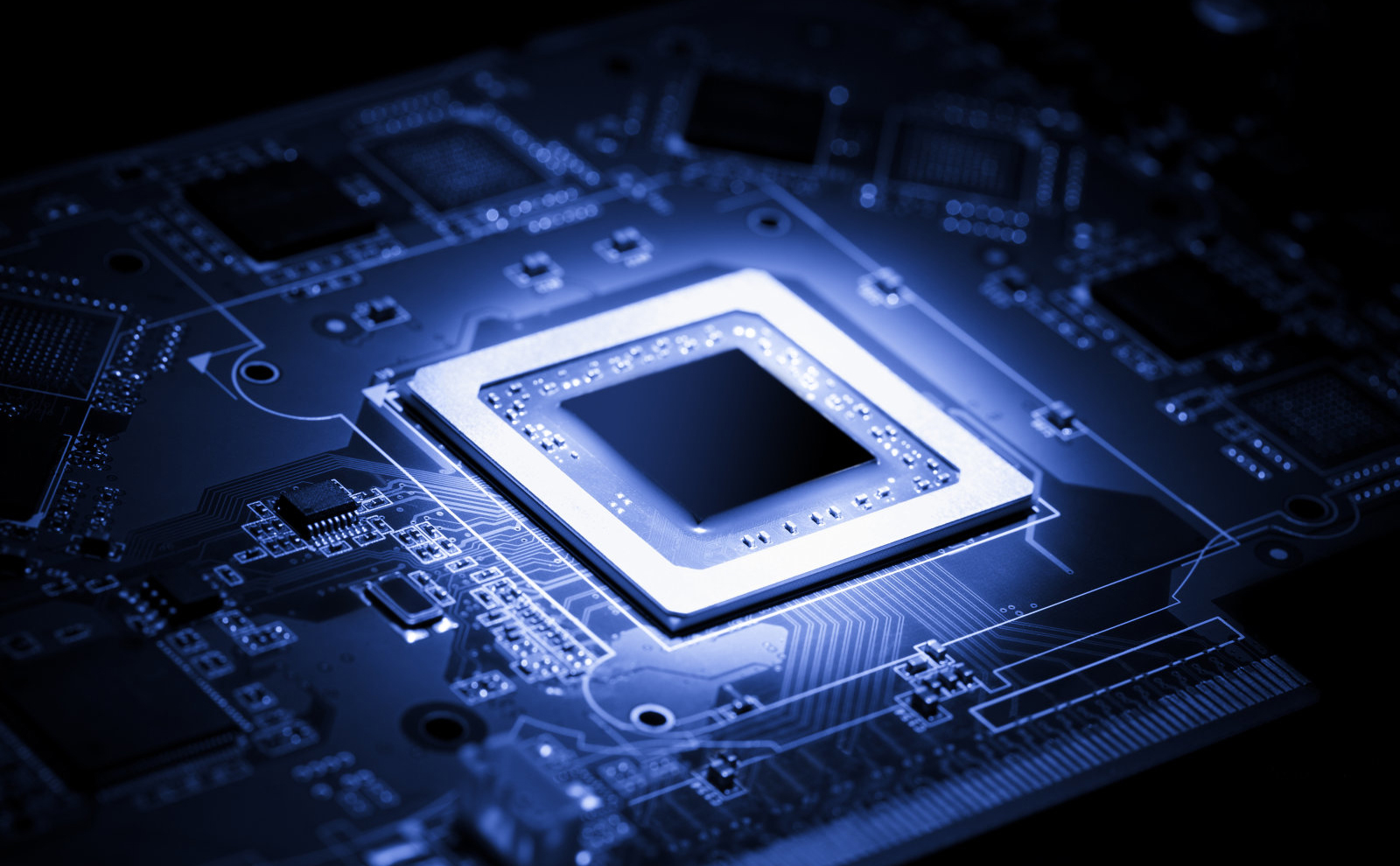 Glowing modern processor. Big illuminated graphic processor surrounding by other electrical components. Special tone image. Low aperture shot, focus on lower part of chip.